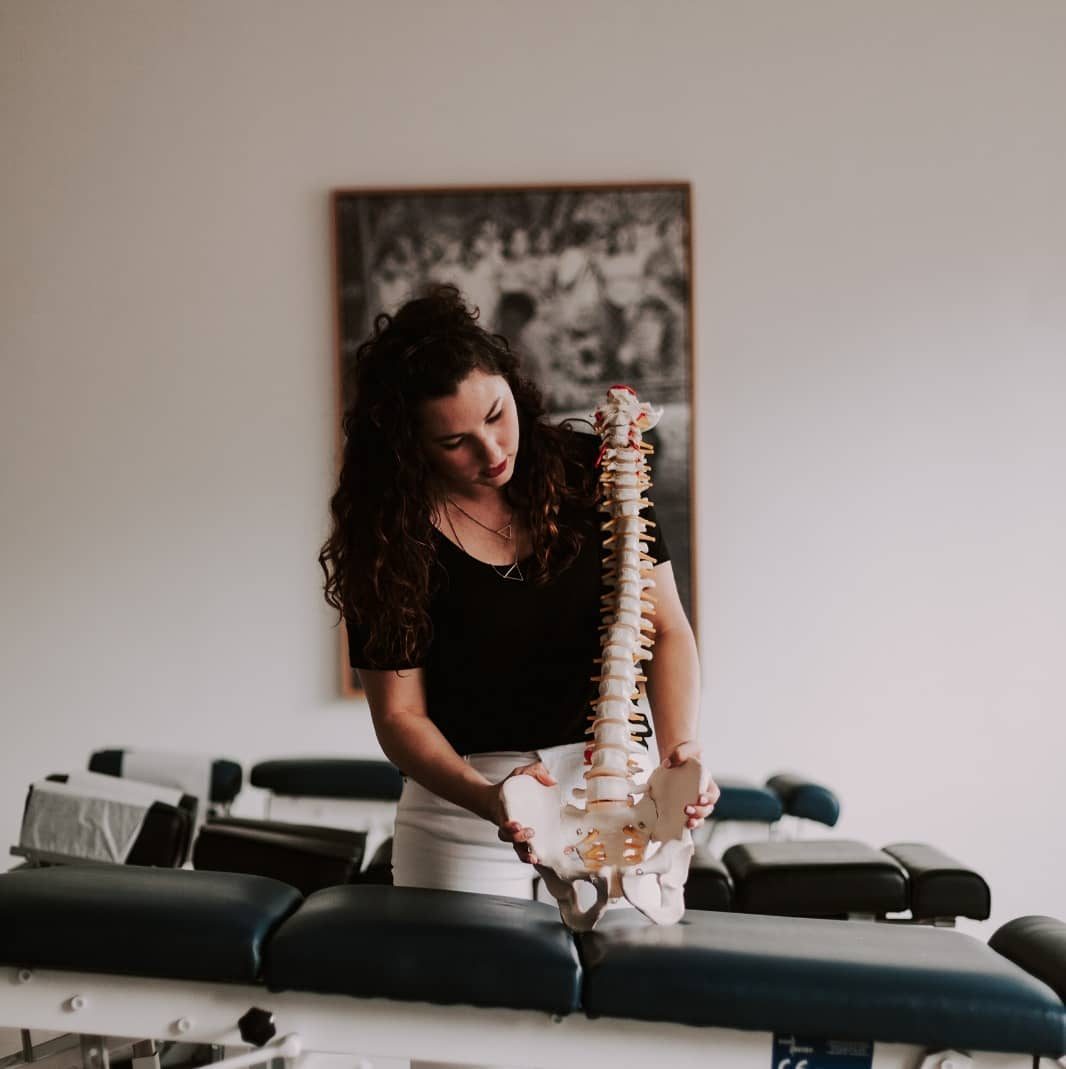 La Dra. Kelli Turelli sosteniendo un modelo de columna en la sala de ajustes de illumINNATE Chiropractic Studio, Barcelona